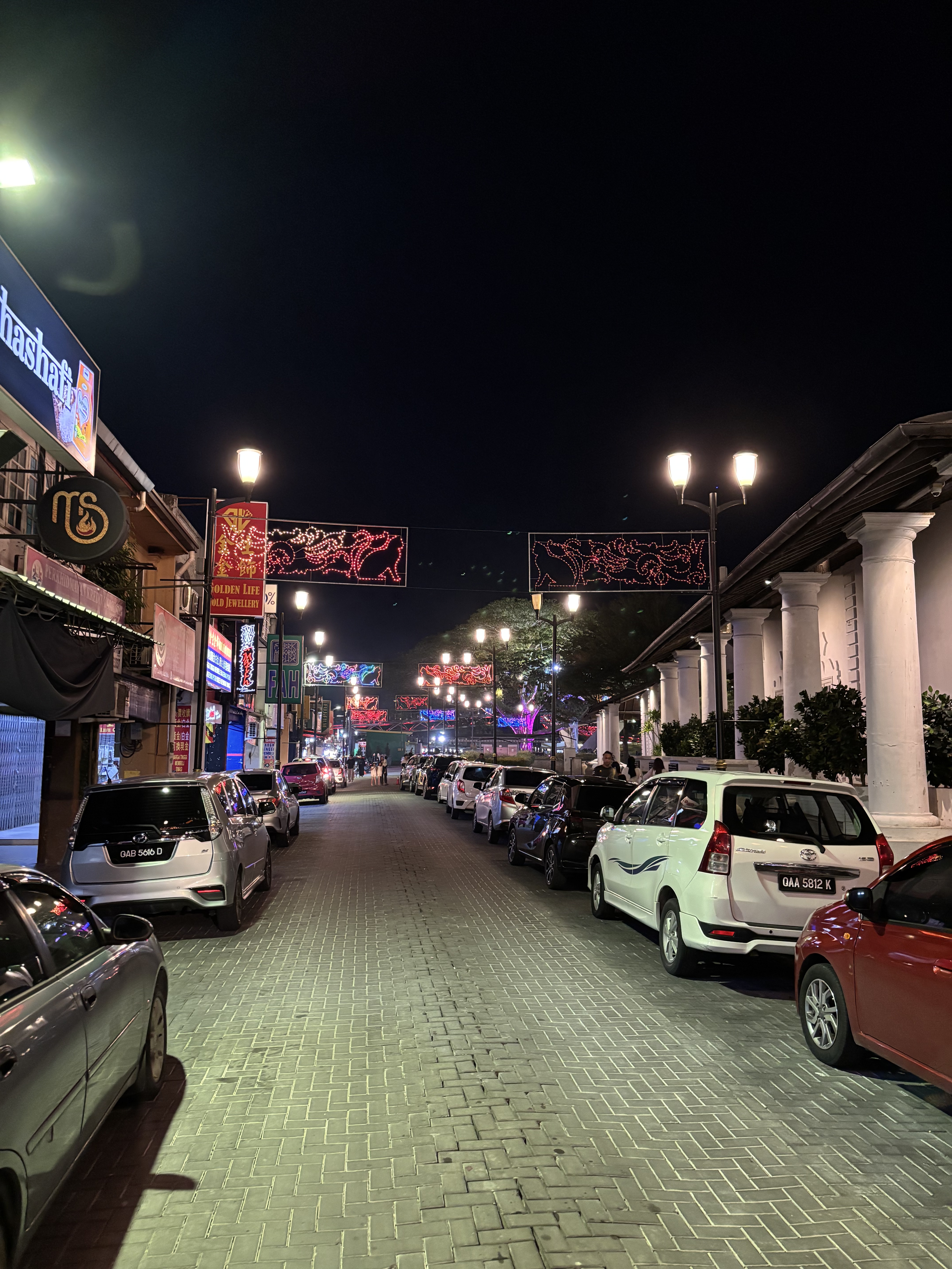 Strada notturna di Kuching con auto parcheggiate e luci decorative sospese