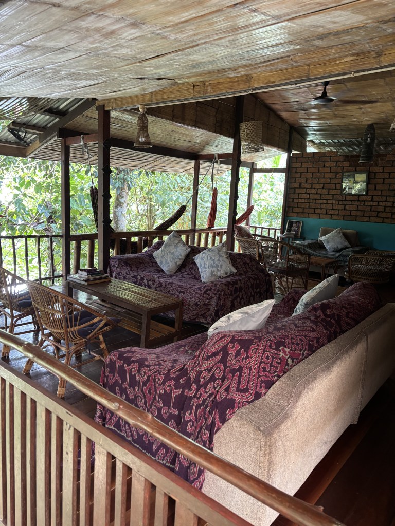 Area salotto aperta sulla veranda del Saloma Villagestay, con divani in rattan e vista sulla foresta pluviale del Borneo