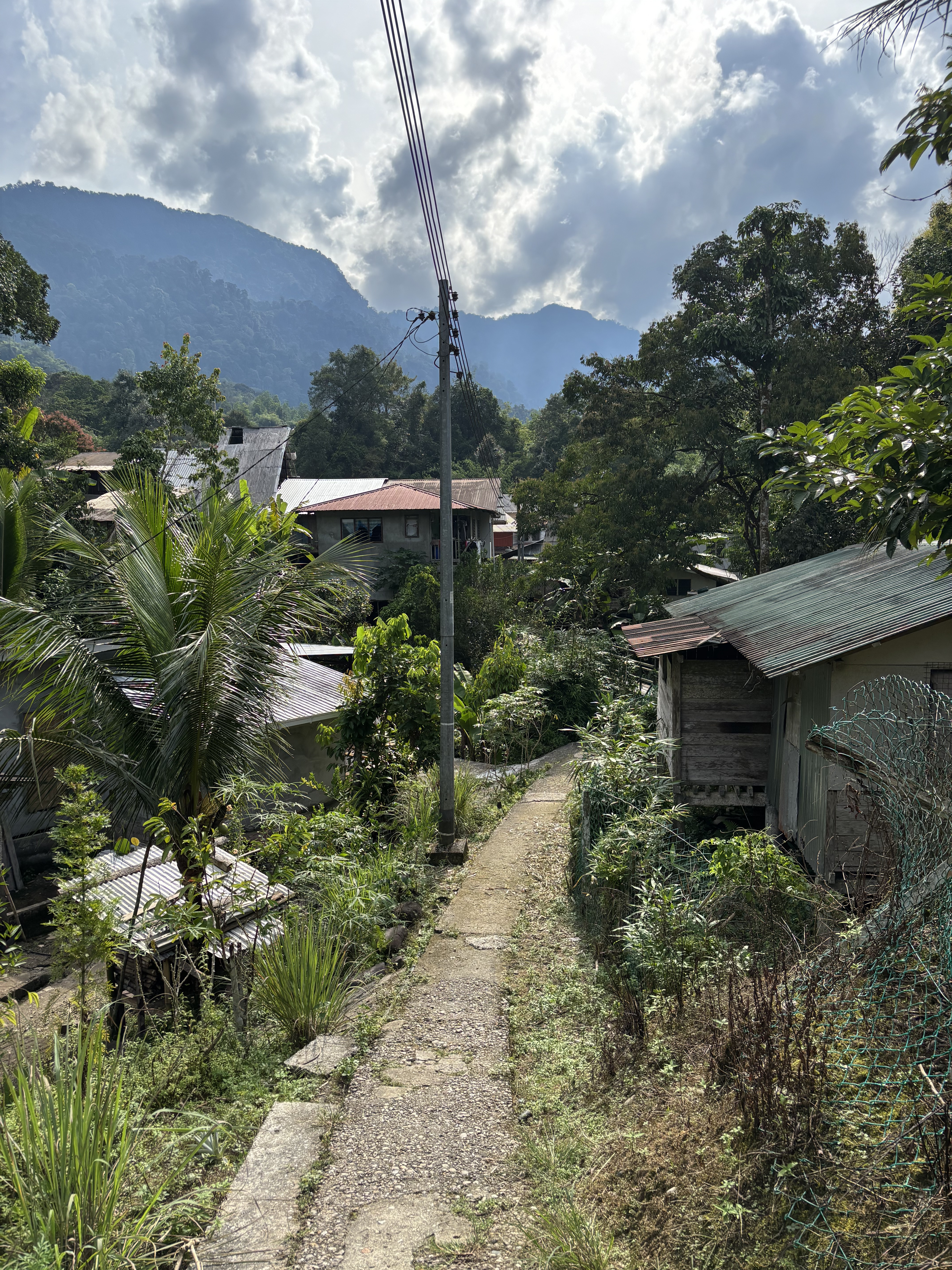 Sentiero tra le case del villaggio con le montagne del Sarawak sullo sfondo